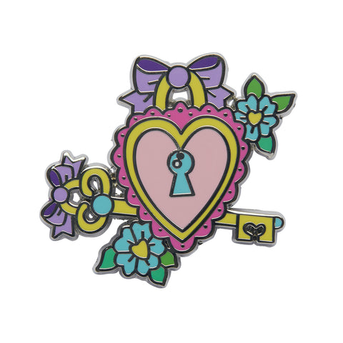 Cute & Spooky by Mimsy Gleeson collaboration collection "Lock and Key" enameled silver metal clutch back pin. A pink ruffled heart with a blue keyhole in the middle surrounded by a large yellow key and two blue flowers with yellow heart shaped pistils.