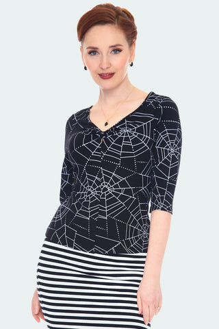 A model wearing a black knit top with an all over spiderweb print. The top has 3/4 length sleeves, a shallow v-neck, and a small keyhole
