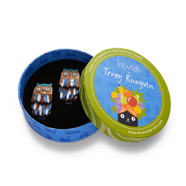 Terry Runyan Collaboration Collection pair of "Feather Dress" layered resin blue and brown owl hair clips, shown in illustrated round box packaging