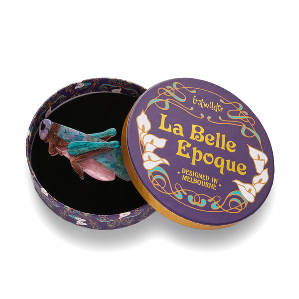 La Belle Époque Collection "Rite of Spring" layered resin blue, green, pink, and brown grasshopper hair clip barrette, shown in illustrated round box packaging
