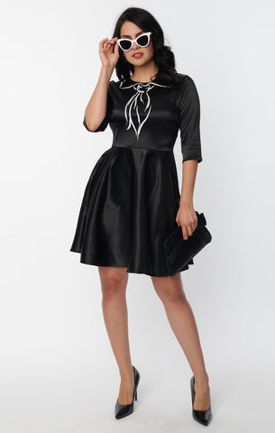 shiny stretch black satin dress featuring a Trompe l'oeil "painted on" scarf and collar printed in contrast bright white, fitted round neckline bodice, 3/4 sleeves, and full just-above-the-knee length skirt, shown on model