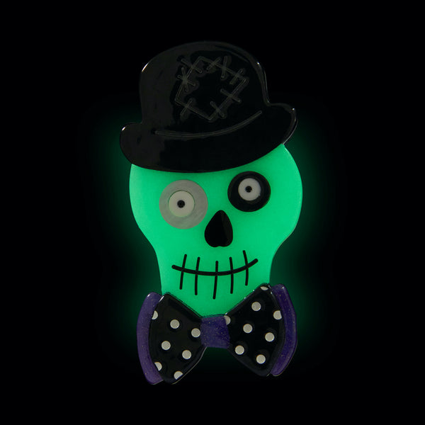 All Hallows' Eve collection "Stan the Bowtie Man" glow-in-the-dark dapper skull wearing bowler hat and bow-tie layered resin brooch, shown glowing