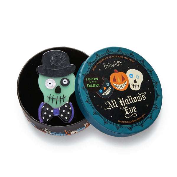All Hallows' Eve collection "Stan the Bowtie Man" glow-in-the-dark dapper skull wearing bowler hat and bow-tie layered resin brooch, shown in illustrated round box packaging