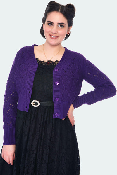 A model wearing a purple knit-in open work cardigan unbuttoned. The cardigan has a diamond design and flower shaped buttons