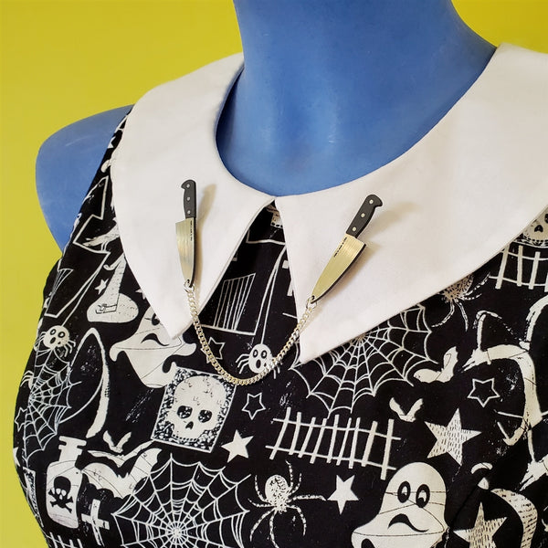 pair opposing black metallic silver laser cut acrylic chef's knife collar clips linked by 4 1/4" silver metal chain, shown on blue mannequin wearing Halloween print dress
